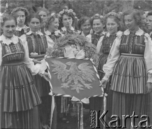 Po 1945, Kanie k. Pruszkowa, woj. warszawskie, Polska.
Dożynki. Mieszkanki wsi w strojach ludowych trzymają wieniec z godłem Polski Ludowej - orłem bez korony.
Fot. Jerzy Konrad Maciejewski, zbiory Ośrodka KARTA

