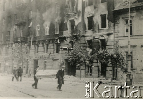 Po 1.09.1939, Warszawa, Polska.
Warszawiacy niosą trumnę obok płonącego budynku. Pl. Trzech Krzyży, na pierwszym planie po prawej stronie oficyna północna Instytutu Głuchoniemych.
Fot. NN, zbiory Ośrodka KARTA, udostępnił Roman Trojanowicz