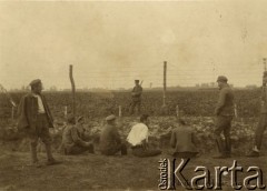 Lipiec - grudzień 1917, Szczypiorno k. Kalisza.
Żołnierze I i II Brygady Legionów, internowani w obozie jenieckim po odmowie złożenia przysięgi na wierność Niemcom. Grupa jeńców na tle ogrodzenia z drutu kolczastego, z tyłu stoi niemiecki wartownik. W prawym dolnym rogu podpis: 