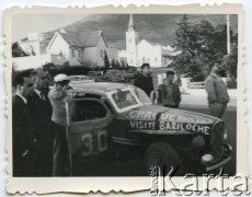 Lata 60., Comodoro Rivadavia, Argentyna.
Rajd samochody w osiedlu kilometro 3. W głębi kościół Santa Lucia.
Fot. NN, zbiory Roberto Carlosa Szymanskiego, reprodukcje cyfrowe w  Bibliotece Polskiej im. Ignacego Domeyki w Buenos Aires (Biblioteca Polaca Ignacio Domeyko) i w Ośrodku KARTA w Warszawie
