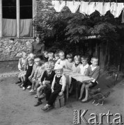 Sierpień 1970, Zagórze lub Kobyłczyce, woj. Katowice, Polska.
Klub Dziecięcy Związku Młodzieży Wiejskiej, zajęcia na świeżym powietrzu - grupa dzieci siedzących przy stole na podwórku razem z wychowawczynią, wyżej suszące sie pranie.
Fot. Kazimierz Seko, zbiory Ośrodka KARTA
