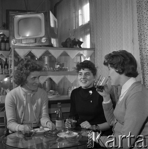 lata 60-te, Kozłowa Góra k/Piekar Śląskich, Polska.
Dom Ludowy pod patronatem Związku Młodzieży Wiejskiej - kawiarnia, młode kobiety siedzące przy stoliku, na półce powyżej stoi telewizor.
Fot. Kazimierz Seko, zbiory Ośrodka KARTA.