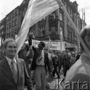 1.05.1976, Katowice, Polska.
Pochód pierwszomajowy, manifestanci z biało-czerwonymi flagami i transparentem, w środku idzie student z Afryki.
Fot. Kazimierz Seko, zbiory Ośrodka KARTA