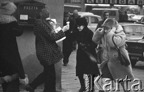 6.01.1975, Warszawa, Polska.
Przechodnie na ulicy w wietrzny dzień, na ścianie budynku wisi skrzynka pocztowa.
Fot. Jarosław Tarań, zbiory Ośrodka KARTA [75-29]
 
