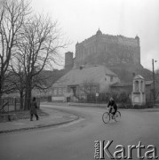 Listopad 1977, Golub-Dobrzyń, Polska
Fragment ulicy, na pierwszym planie kobieta jadąca na rowerze, za nią kapliczka, w tle na wzgórzu zamek.
Fot. Jarosław Tarań, zbiory Ośrodka KARTA [77-29]

