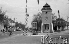 Maj 1979, Nasielsk, woj. ciechanowskie, Polska.
Fragment miasta - Herb Nasielska, flagi, rowerzysta. W oddali widoczne są przejeżdżające samochody, drzewa oraz zabudowa mieszkalna. 
Fot. Jarosław Tarań, zbiory Ośrodka KARTA [79-52] 
