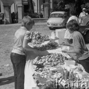 Sierpień 1979, Wysokie Mazowieckie, woj. łomżyckie, Polska.
Odpust - dzieci przy straganie z obwarzankami. W oddali widoczny jest samochód marki Syrena oraz brama prowadząca do kościoła. 
Fot. Jarosław Tarań, zbiory Ośrodka KARTA [79-6]