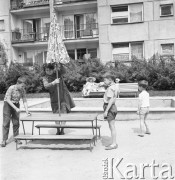 6.06.1968, Warszawa, Polska.
Dzień pracy dozorczyni - kobieta montuje parasol przeciwsłoneczny na placu zabaw, na drugim planie kobieta opalająca się na ławce.
Fot. Jarosław Tarań, zbiory Ośrodka KARTA
