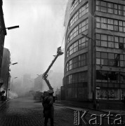 23.05.1968, Warszawa, Polska.
Ćwiczenia strażackie w Powszechnym Domu Towarowym Praga. Milicjant obserwuje strażaków gaszących pożar. W oddali widoczne są wozy strażackie oraz dym unoszący się nad ulicą. 
Fot. Jarosław Tarań, zbiory Ośrodka KARTA