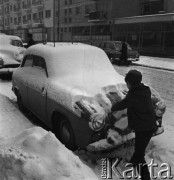 02.01.1968, Warszawa, Polska.
Centrum miasta zimą - chłopiec odśnieża maskę auta. Na drugim planie widoczne są budynki z balkonami oraz zaparkowane na poboczu samochody.
Fot. Jarosław Tarań, zbiory Ośrodka KARTA