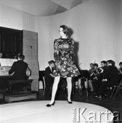 26.02.1968, Warszawa, Polska.
Pokaz setnej kolekcji firmy CORA zaprojektowanej przez Jadwigę Grabowską. Modelka w krótkiej sukience w motywy roślinne, w tle akompaniatorzy.
Fot. Jarosław Tarań, zbiory Ośrodka KARTA