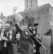 01.05.1968, Warszawa, Polska.
Pochód pierwszomajowy w centrum Warszawy. Starszy pan niesie na barana dziewczynkę przebraną w krakowski strój ludowy. Obok starsza pani z chłopcem trzymającym szturmówkę, w tle Domy Towarowe 