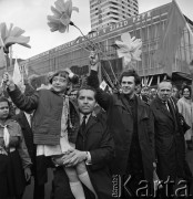 01.05.1968, Warszawa, Polska.
Pochód pierwszomajowy w centrum Warszawy, manifestanci ze sztucznymi kwiatami. Na pierwszym planie mężczyzna z dziewczynką na rękach, w tle Domy Towarowe 