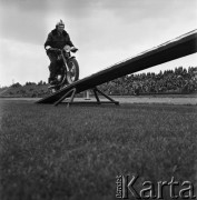 1968, Nowa Iwiczna, woj. Warszawa, Polska.
Szkoła Podoficerska MO Służby Ruchu Drogowego, pokaz jazdy akrobatycznej na motocyklu, w tle widzowie na trybunach.
Fot. Jarosław Tarań, zbiory Ośrodka KARTA