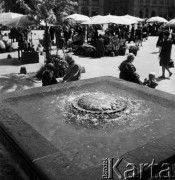 1968, Kraków, Polska.
Rynek Główny w Krakowie. Na pierwszym planie dziecko bawiące się pod zabytkową fontanną, w tle tłum ludzi spacerujących po rynku i stragany z kwiatami.
Fot. Jarosław Tarań, zbiory Ośrodka KARTA