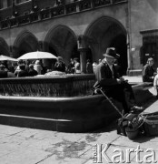 1968, Kraków, Polska.
Rynek Główny w Krakowie. Na pierwszym planie elegancki mężczyzna siedzący na zabytkowej fontannie, w tle tłum ludzi zgromadzony pod Sukiennicami.
Fot. Jarosław Tarań, zbiory Ośrodka KARTA