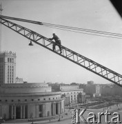 19.03.1963, Warszawa, Polska.
Mężczyzna wspinający się po ramieniu dźwiga podczas kontroli dźwignic na budowie Osiedla Emilia. W tle Sala Kongresowa Pałacu Kultury i Nauki.
Fot. Jarosław Tarań, zbiory Ośrodka KARTA [63-107]


