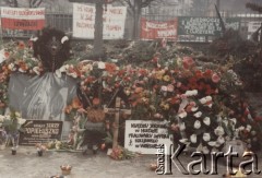 3.11.1984, Warszawa, Polska.
Pogrzeb księdza Jerzego Popiełuszki w Kościele św. Stanisława Kostki na warszawskim Żoliborzu - kwiaty złożone na grobie tragicznie zmarłego księdza. Na drugim planie widoczne są transparenty. 
Fot. NN, zbiory Ośrodka KARTA
