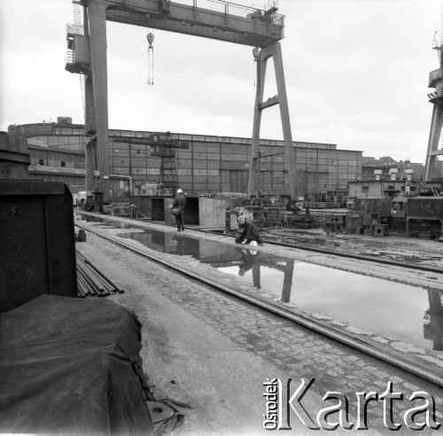 Około 1966, Gdańsk, Polska.
Stocznia Gdańska (od 15.04.1967 Stocznia Gdańska im. Lenina). Fotoreporter ustawia kadr przy jednej z pochylni. W tle suwnica oraz budynki stoczniowe.
Fot. Edward Grochowicz, zbiory Ośrodka KARTA.