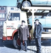 Lata 70. lub 80., Warszawa, Polska.
Fotografia reklamowa dla Przedsiębiorstwa Międzynarodowych Przewozów Samochodowych PEKAES - dwaj pracownicy przedsiębiorstwa przy ciężarówce załadowanej transportem w postaci modeli auta Fiat 125p.
Fot. Edward Grochowicz, zbiory Ośrodka KARTA.