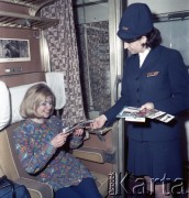 Lata 70. lub 80., Polska.
Fotografia reklamowa dla Centralnego Biura Obsługi Podróżnych PKP POLRES. Pracownica PKP w przedziale pociągu prezentuje podróżnej folder turystyczny o Krakowie.
Fot. Edward Grochowicz, zbiory Ośrodka KARTA.
